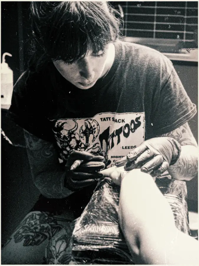 María tatuando una pierna, fotografía antigua en blanco y negro.