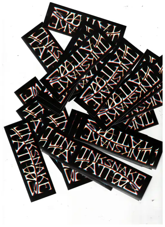 Pegatinas del rótulo de InkSnake Tattoos en dorado sobre negro, esparcidas.