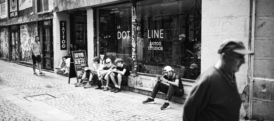 Fachada de un estudio de tatuaje en una calle empedrada, con gente sentada fuera.