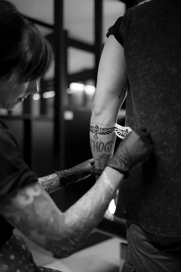 María tatuando un antebrazo de pie, en blanco y negro.