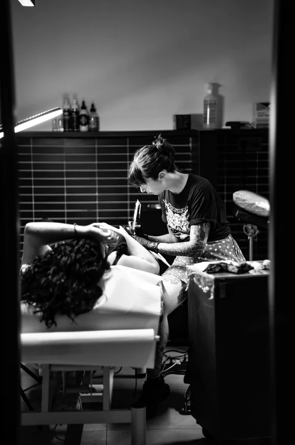 María tatuando a un cliente tumbado en la camilla.