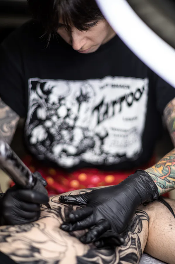 María tatuando con guantes negros, detalle de las manos y la máquina.