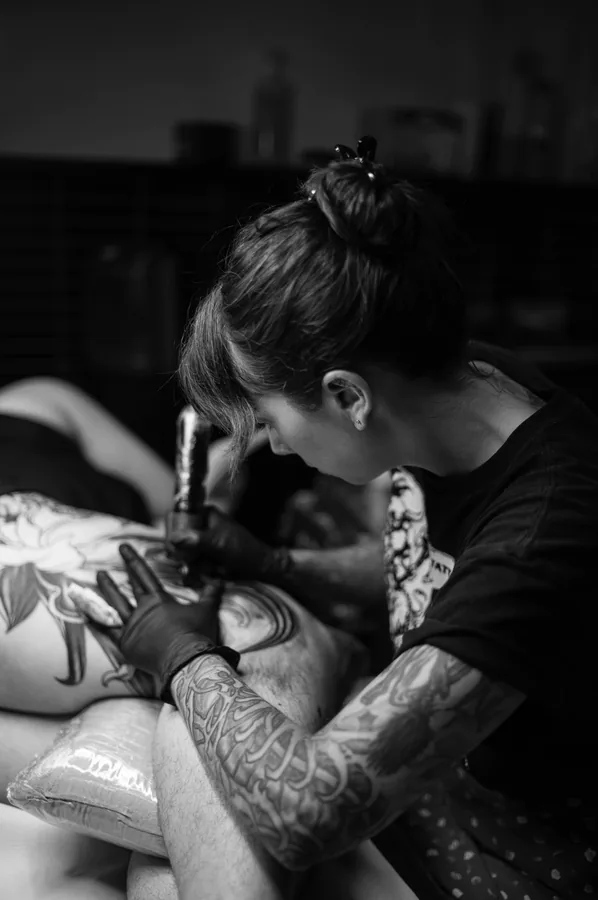 María concentrada tatuando un brazo, en blanco y negro.