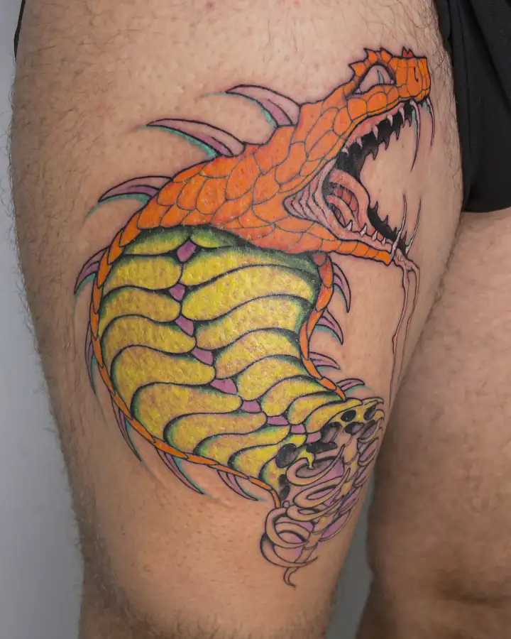 En el muslo, una criatura de fauces abiertas en naranja y amarillo, a color y de contornos muy marcados.