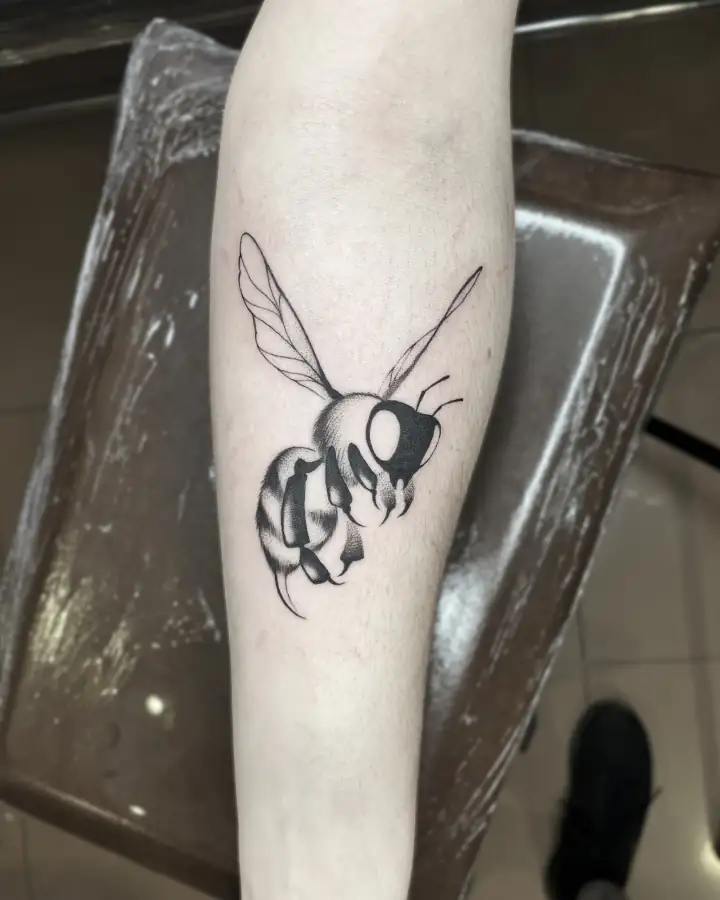 Antebrazo con una abeja en vuelo: alas a línea fina y cuerpo sombreado en black & grey.