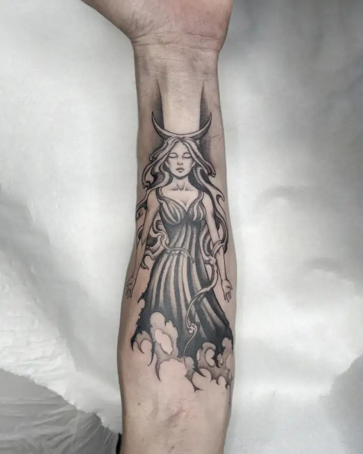 Antebrazo con una figura femenina de vestido largo bajo una luna creciente, sobre nubes, en black & grey.