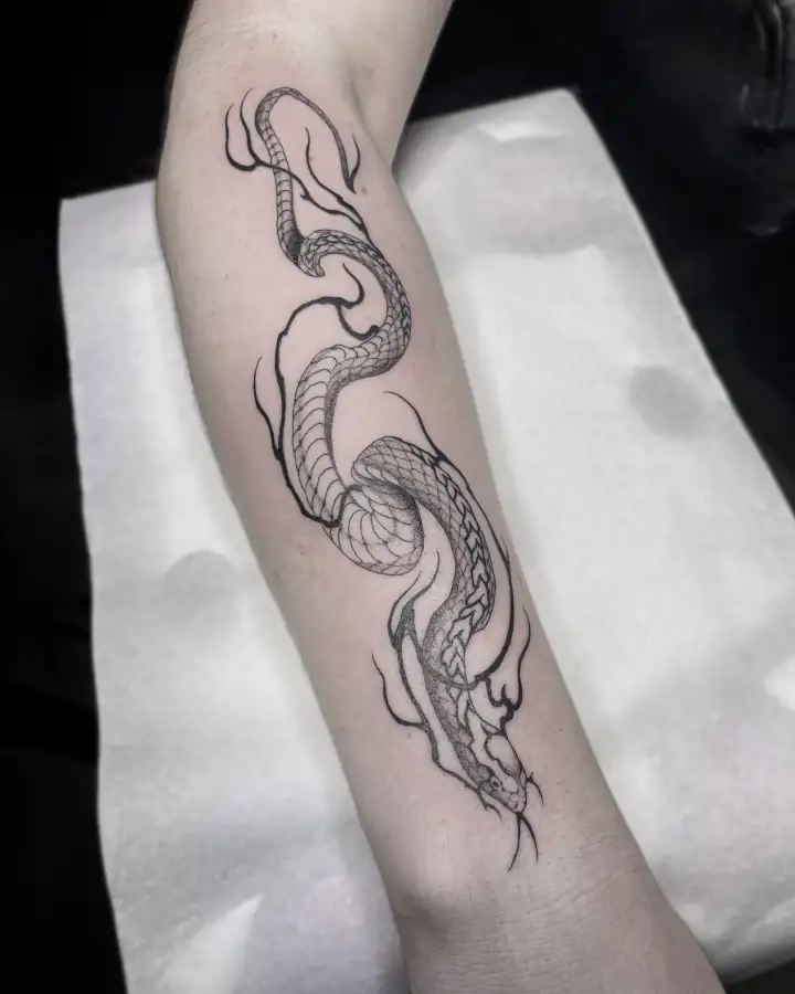 Antebrazo recorrido por una serpiente de escamas menudas entre volutas de humo, en línea fina con relleno en dotwork.