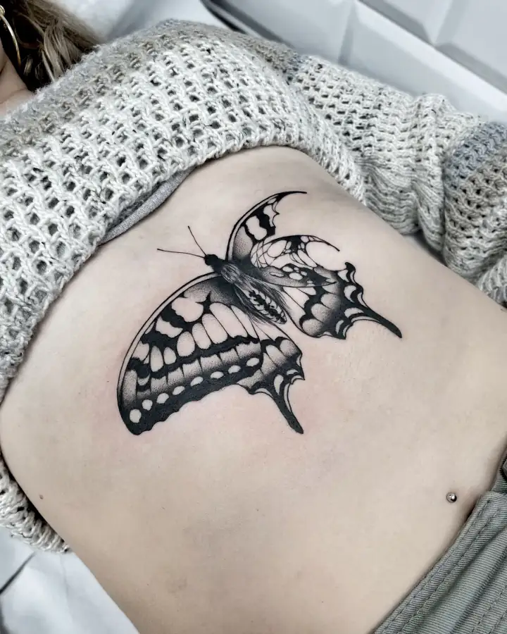 Vientre con una mariposa grande de alas moteadas y nervadas, en blackwork con degradados en puntillismo.