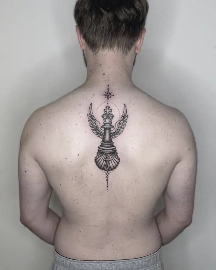 En el centro de la espalda, una pieza de ajedrez alada rematada en corona, entre estrellas, en línea fina y dotwork.
