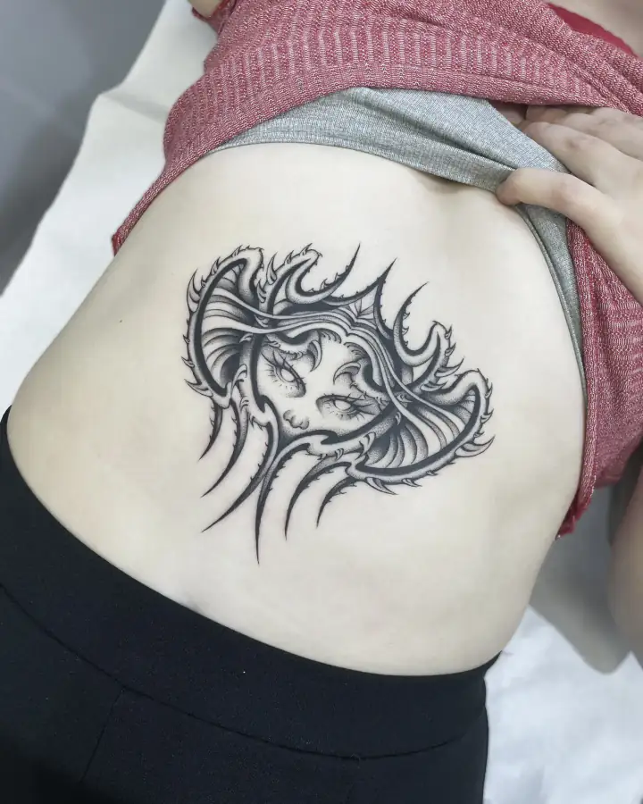 Zona lumbar: un rostro femenino envuelto en púas y melena, en black & grey de aire neotribal.