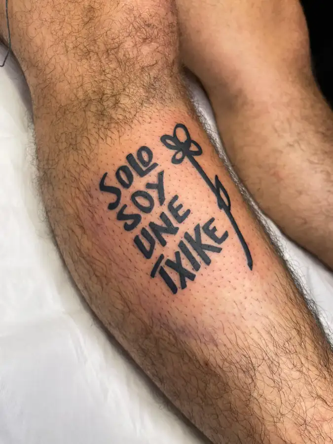 Pantorrilla con la frase «Solo soy une txike» en lettering de trazo grueso junto a una flor de tallo largo.