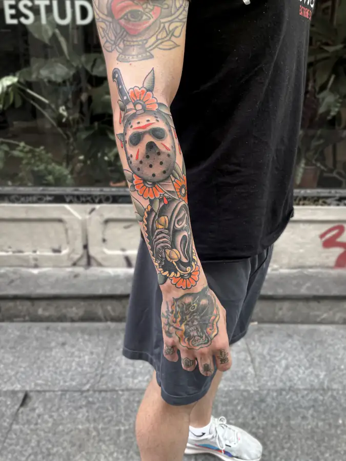 Manga entera de perfil, a color: máscaras de terror y flores naranjas de contorno grueso, en estilo tradicional.