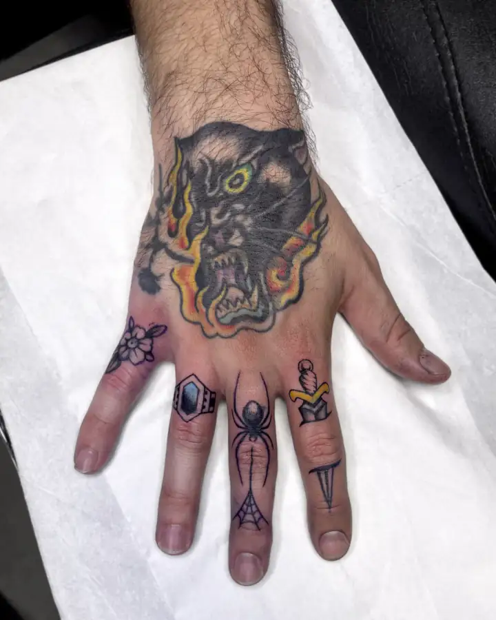 Dorso de la mano con una pantera entre llamas, a color y de corte tradicional, más piezas pequeñas en los dedos.