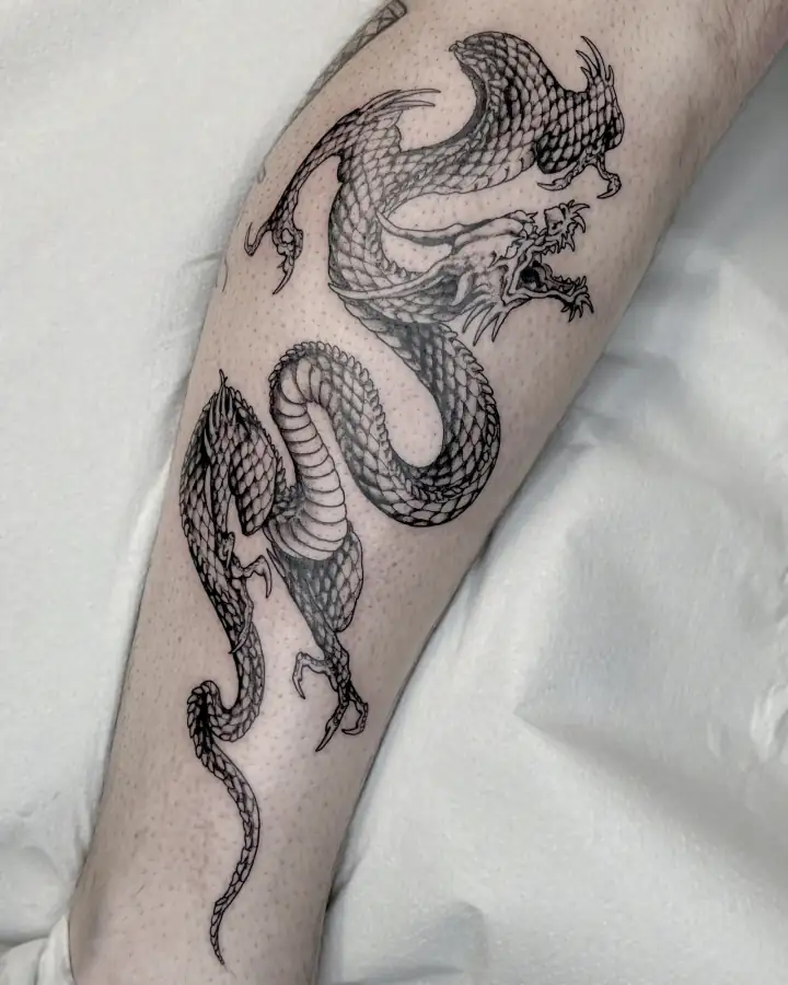 Por la pantorrilla serpentea un dragón oriental de escamas menudas, tatuado a línea fina con grises muy suaves.
