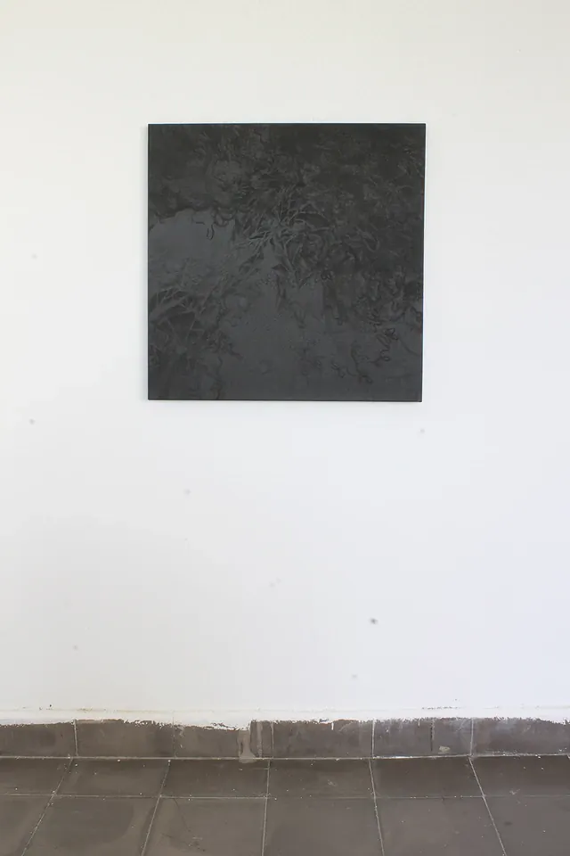 Pintura oscura casi cuadrada colgada en una pared blanca sobre un zócalo de baldosas; en su mitad superior se distinguen hojas y trazos grises.