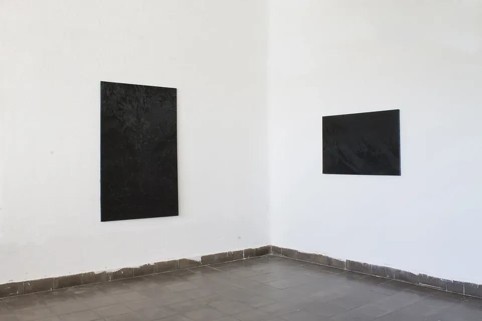Esquina de una sala de paredes blancas y suelo de baldosas con dos pinturas oscuras colgadas, una vertical a la izquierda y otra horizontal a la derecha.