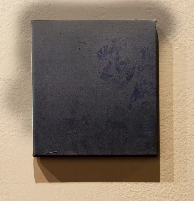Lienzo casi cuadrado azul oscuro colgado en una pared crema, con siluetas de hojas azules en la esquina superior derecha.