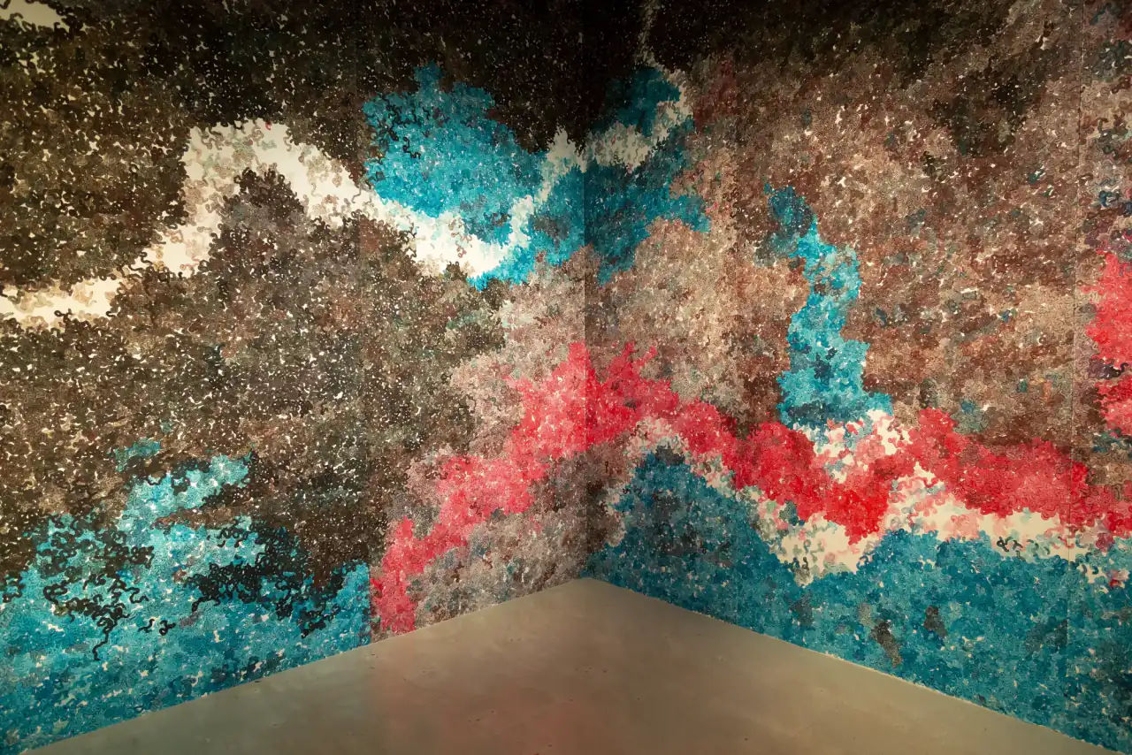 MUR MUR, pintura sobre papel (2018). Esquina de sala cubierta de pintura sobre papel: formas turquesa y rojas en la base, una franja blanca arriba y masas pardas y oscuras.