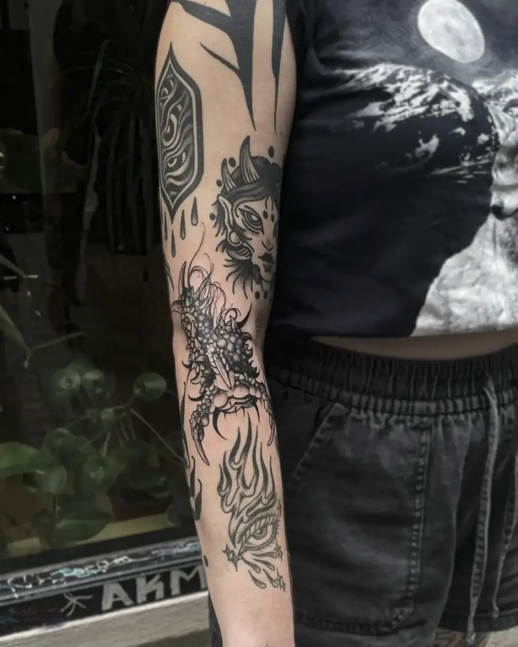 Brazo entero con piezas sueltas en blackwork: escudo ornamental, rostro felino, garra escamosa y llamas del hombro a la muñeca.