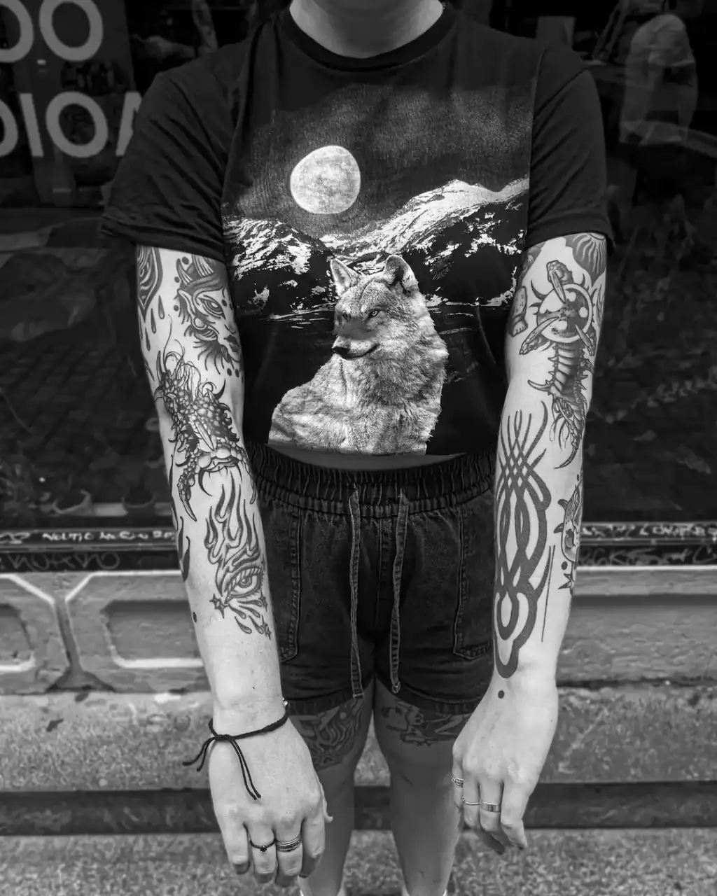 Los dos brazos tatuados de frente, con llamas, insectos y trazos neotribales en negro; foto en blanco y negro.