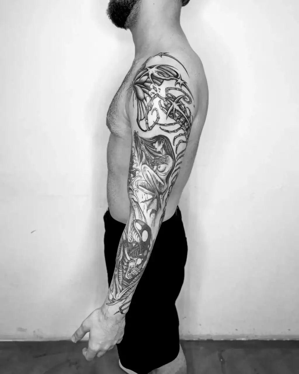 Manga completa de brazo vista de perfil: formas orgánicas, una figura alada y un cráneo en black & grey de sombreado suave.