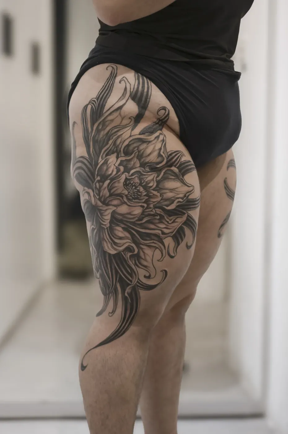 Cadera y muslo de perfil con un gran crisantemo de hojas curvadas que baja hasta la rodilla, en black & grey.