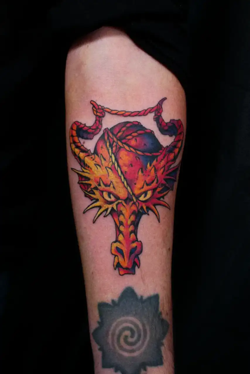 Brazo con una cabeza de dragón de cuernos, cuerda y llamas, a color de contorno grueso; debajo, una mancha negra con espiral.