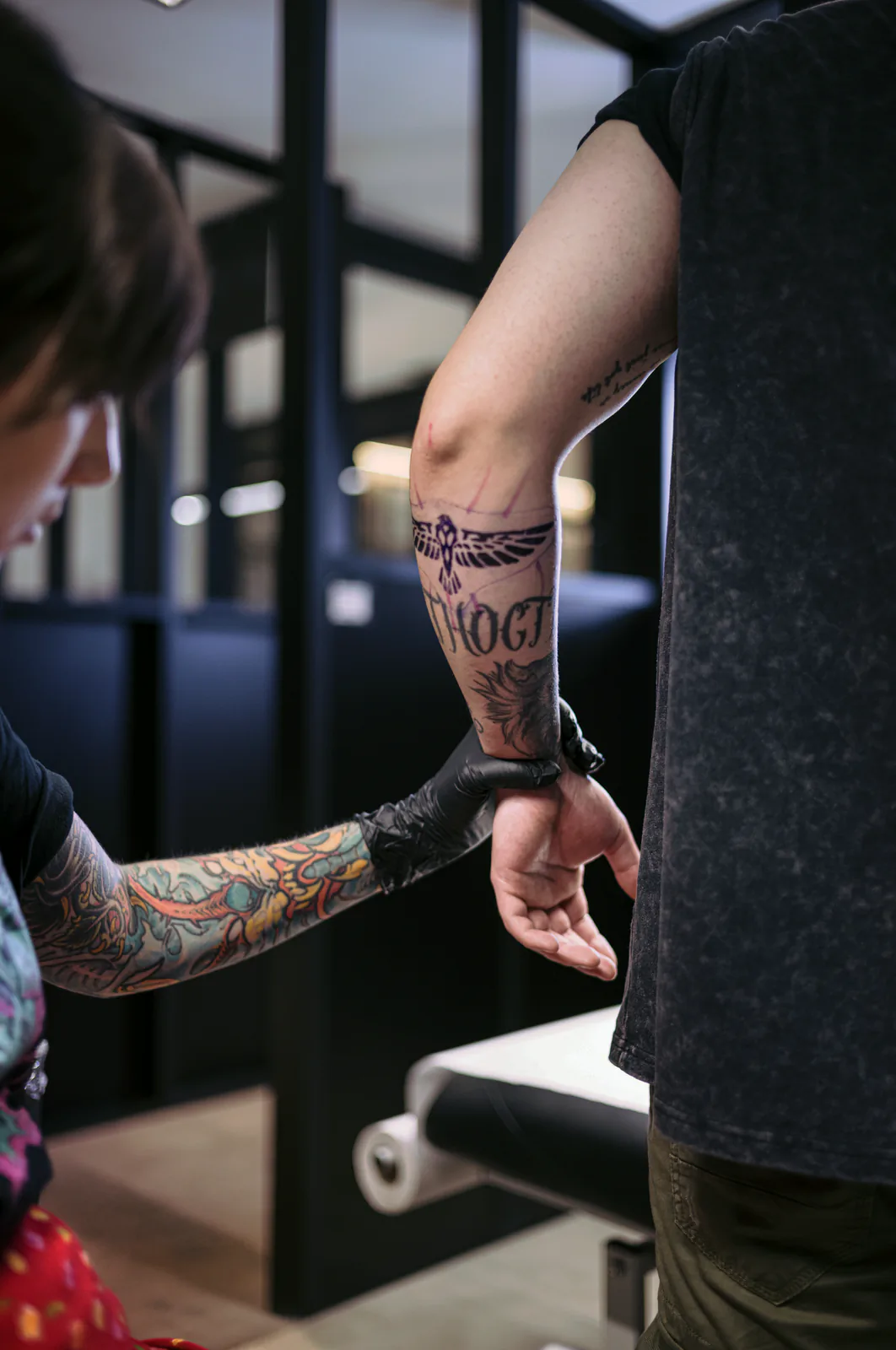 Brazo tatuado a color extendido en el estudio, con una reja metálica al fondo.