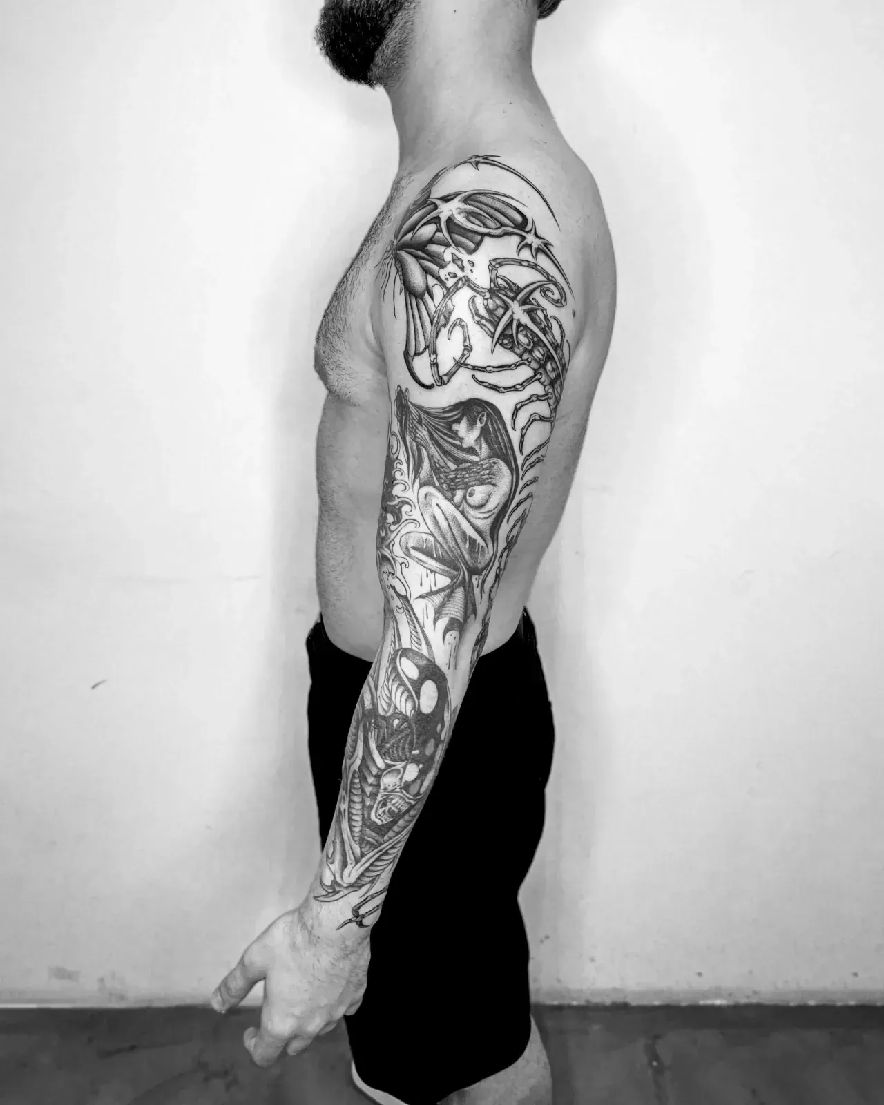 Manga completa en blackwork vista de perfil: una figura femenina y una criatura fantástica bajan del hombro a la muñeca del brazo izquierdo. Fotografía en blanco y negro.