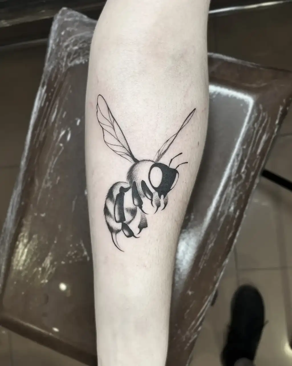 En el antebrazo, una abeja en vuelo con las alas de línea fina y el cuerpo en black & grey de sombreado suave.