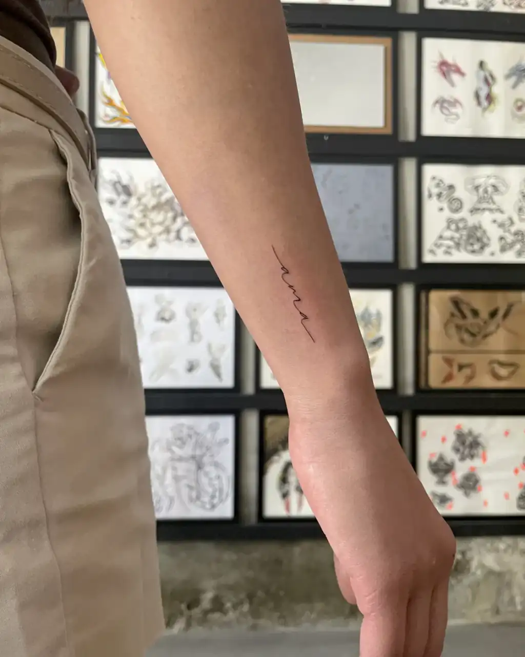 En el antebrazo, una palabra corta escrita en cursiva minúscula, lettering de línea fina.