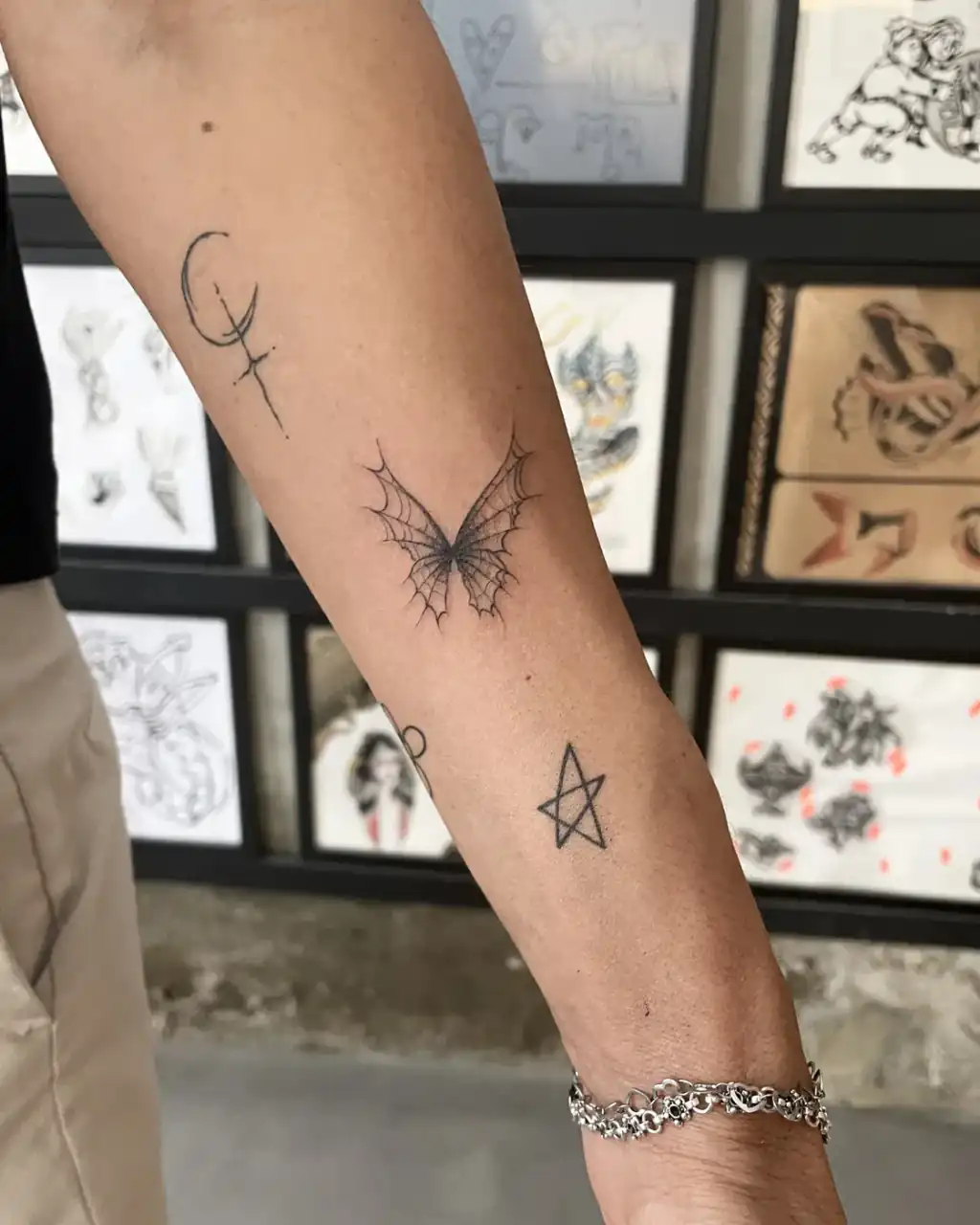 Antebrazo sembrado de piezas menudas: luna creciente, mariposa de alas de telaraña y estrella, todas a línea fina.