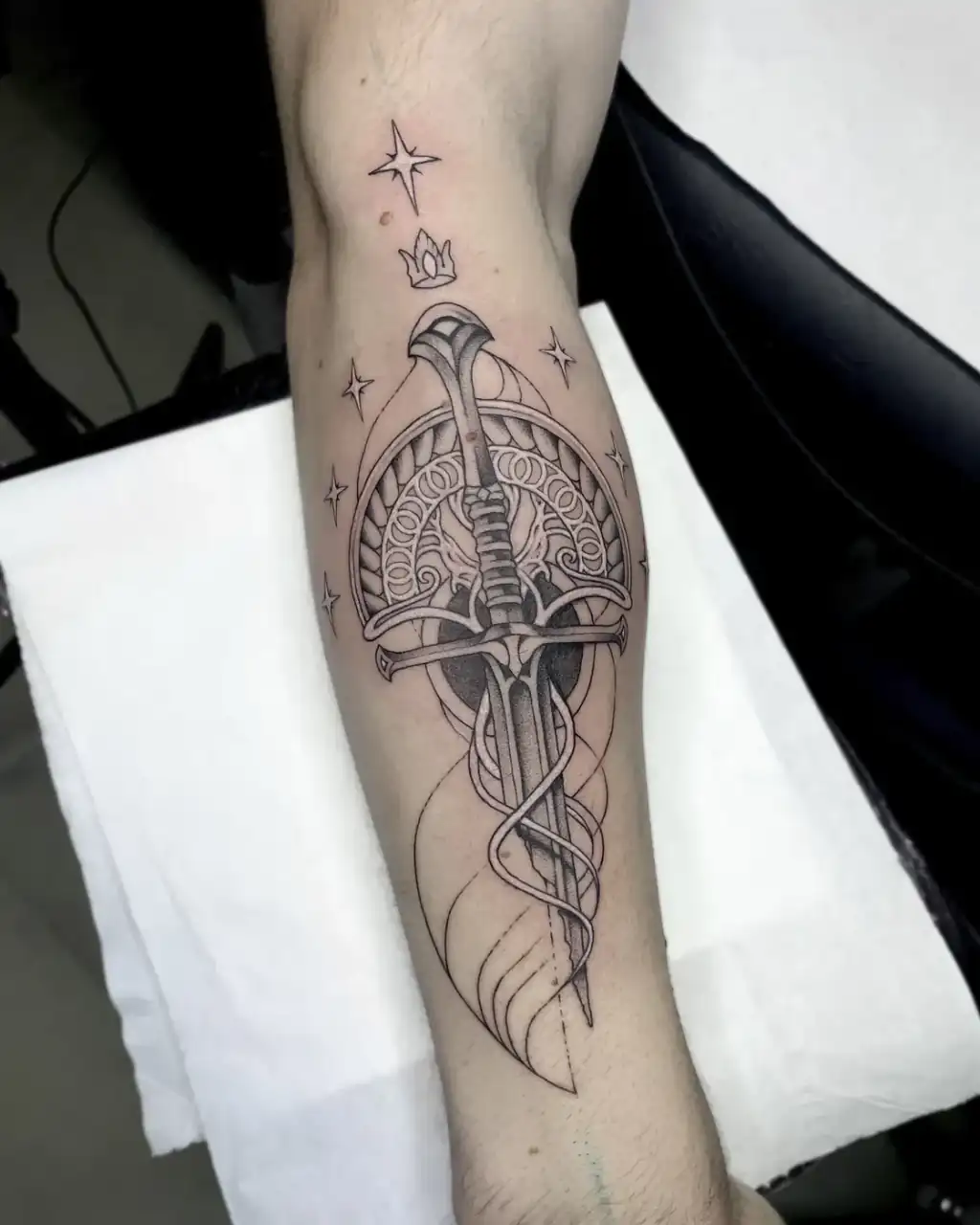 Antebrazo: una espada sobre un arco ornamental rodeada de destellos, en línea fina con sombreado suave.