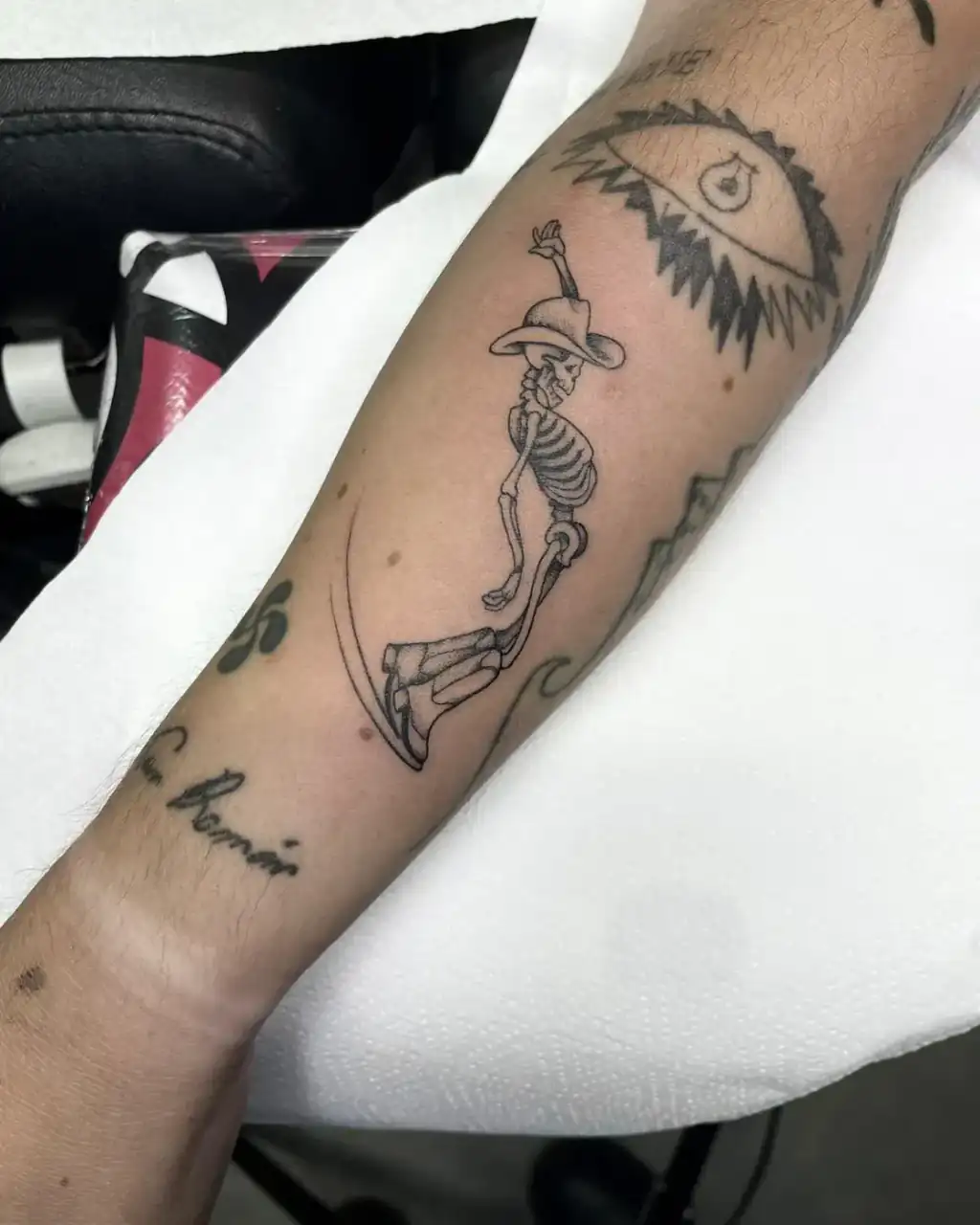 Antebrazo: un esqueleto con sombrero de ala ancha camina sobre una línea curva, todo en línea fina.