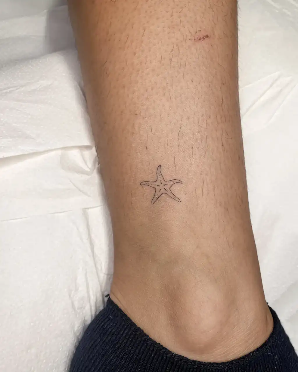 Sobre el tobillo, una estrella de mar diminuta de línea fina con el centro punteado.