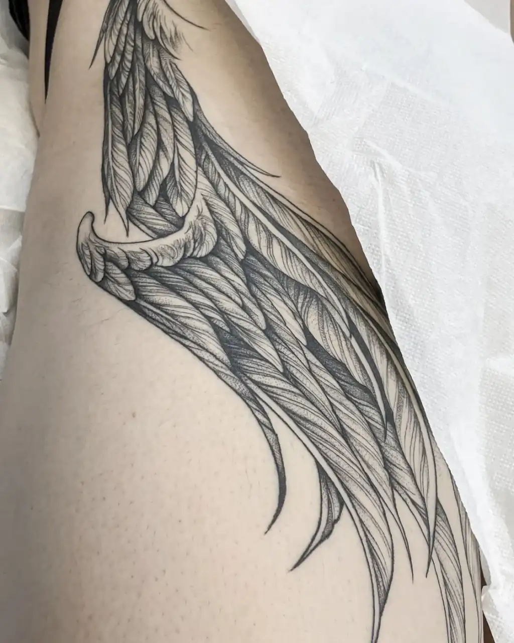 Costado con una gran ala de plumas extendida, dibujada a línea fina y sombreada a base de puntos en dotwork.