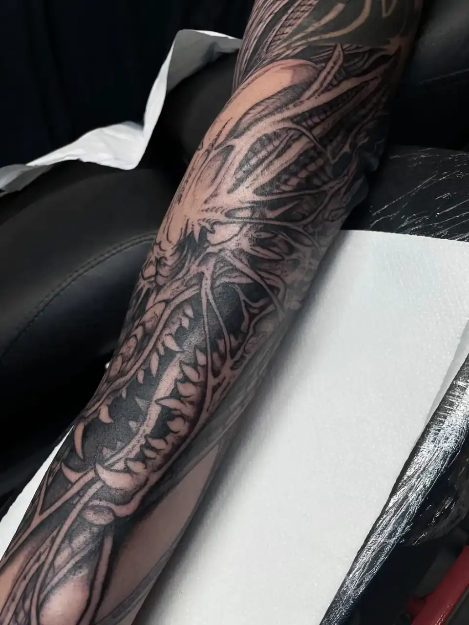 Manga de antebrazo con formas biomecánicas y unas fauces de colmillos, en black & grey de contrastes muy marcados.