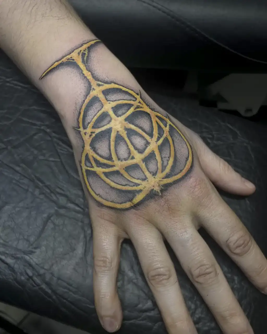 Dorso de la mano cubierto de negro sólido y atravesado por un entramado de círculos en amarillo, de aire ornamental.