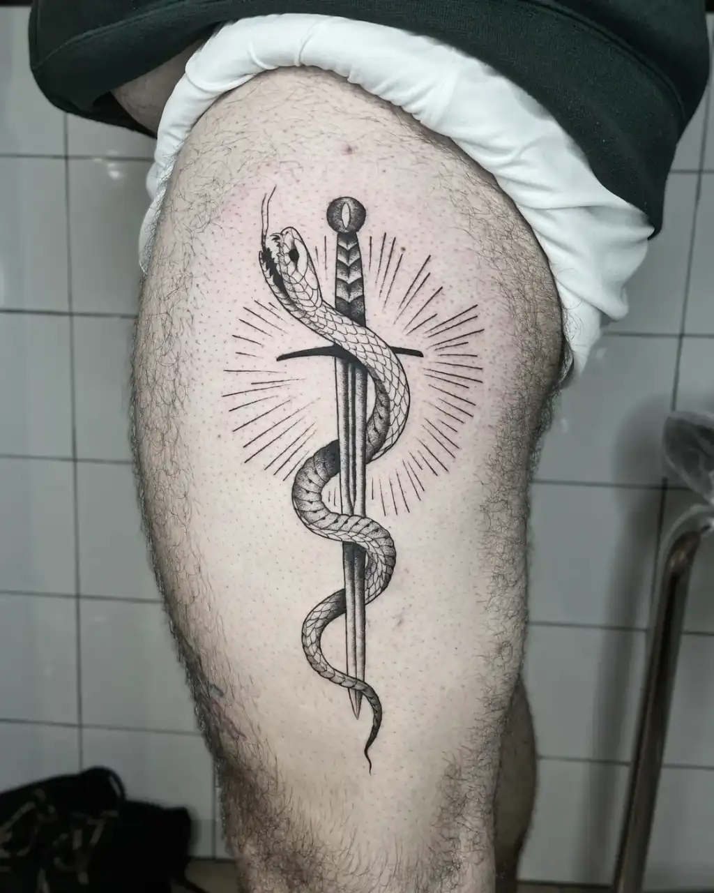 Muslo con una daga abrazada por una serpiente sobre un estallido de rayos, a línea fina y sombreado en puntillismo.