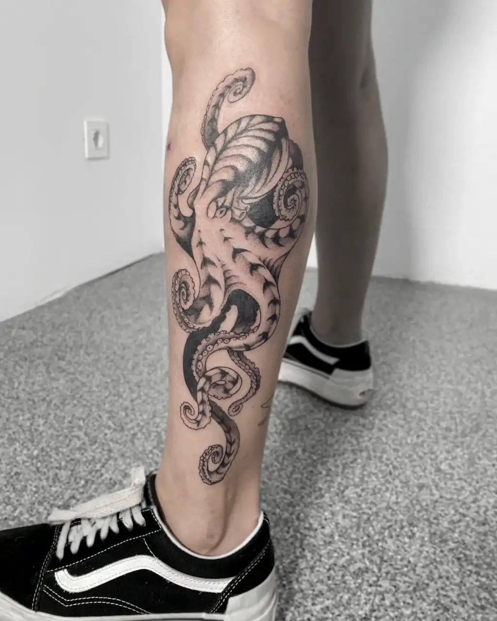 Por la pantorrilla baja un pulpo de tentáculos enroscados, en black & grey con línea fina y sombras suaves.