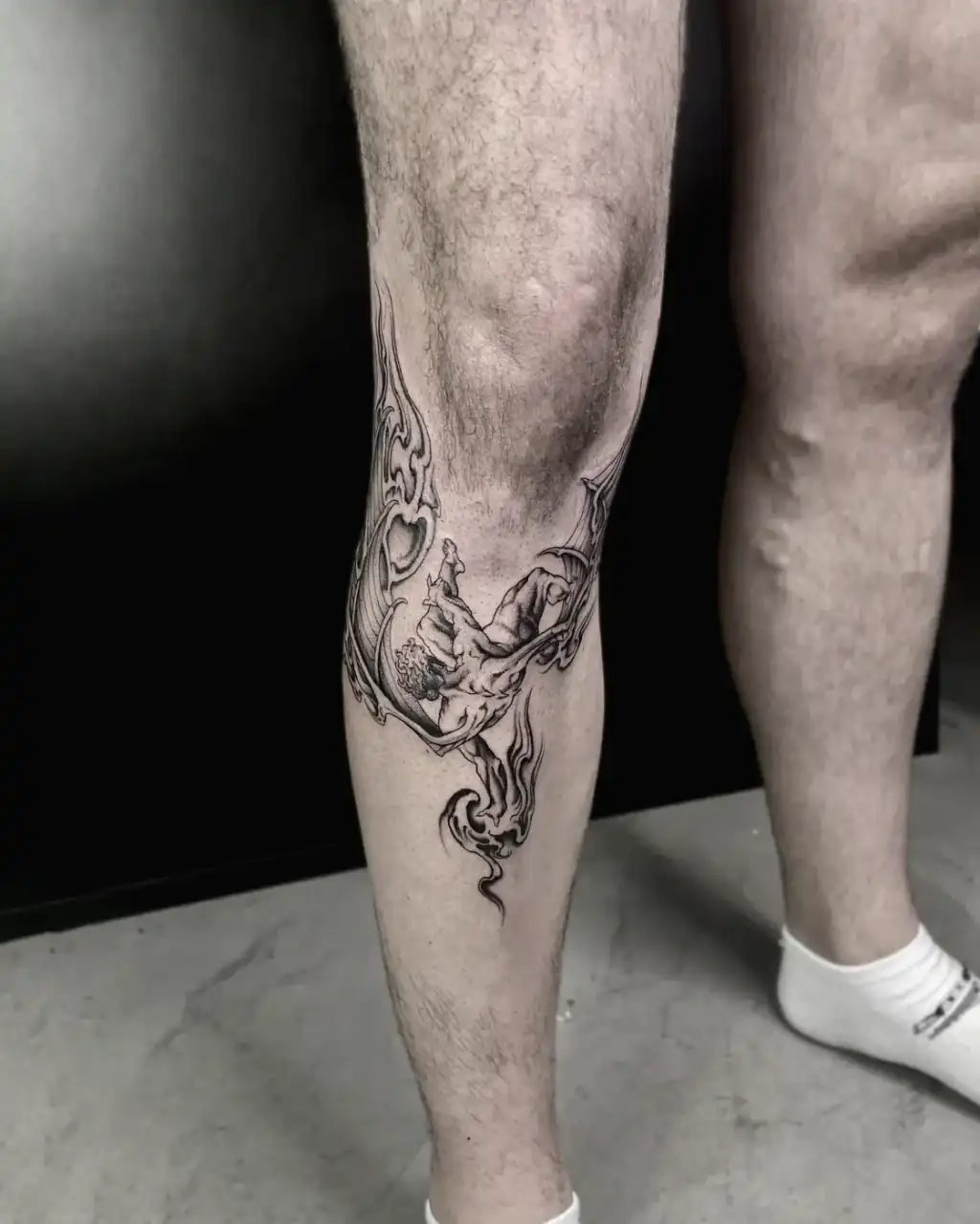 Pierna con una pieza envolvente de línea fina: volutas y llamas que rodean la rodilla y bajan por la pantorrilla.