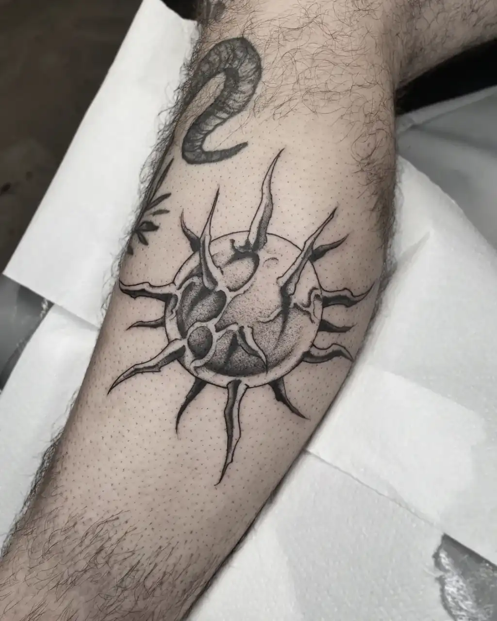 Pantorrilla: un sol de rayos puntiagudos con el disco trabajado en dotwork.