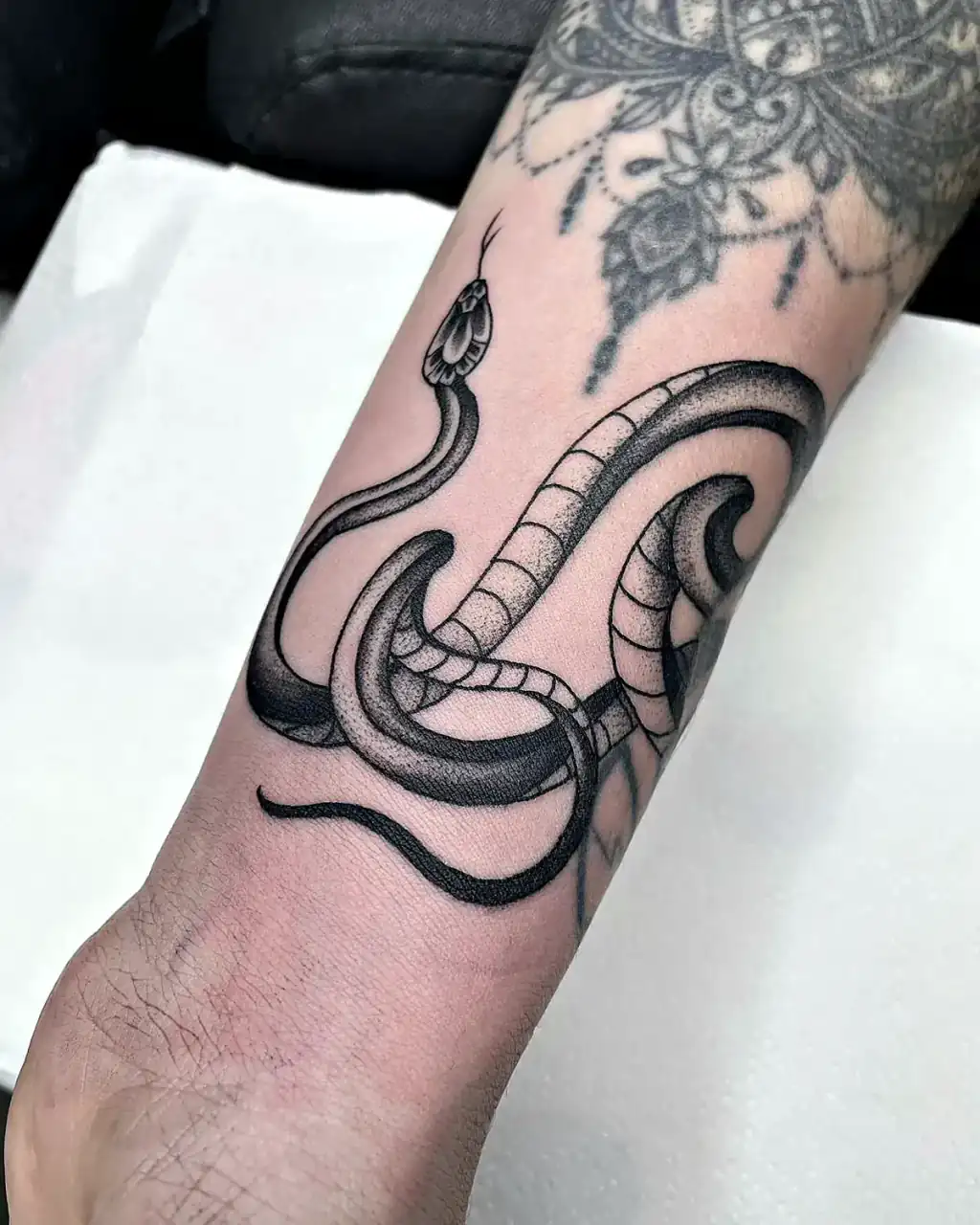 Serpiente enroscada en blackwork puntillista junto a mandala en la muñeca.