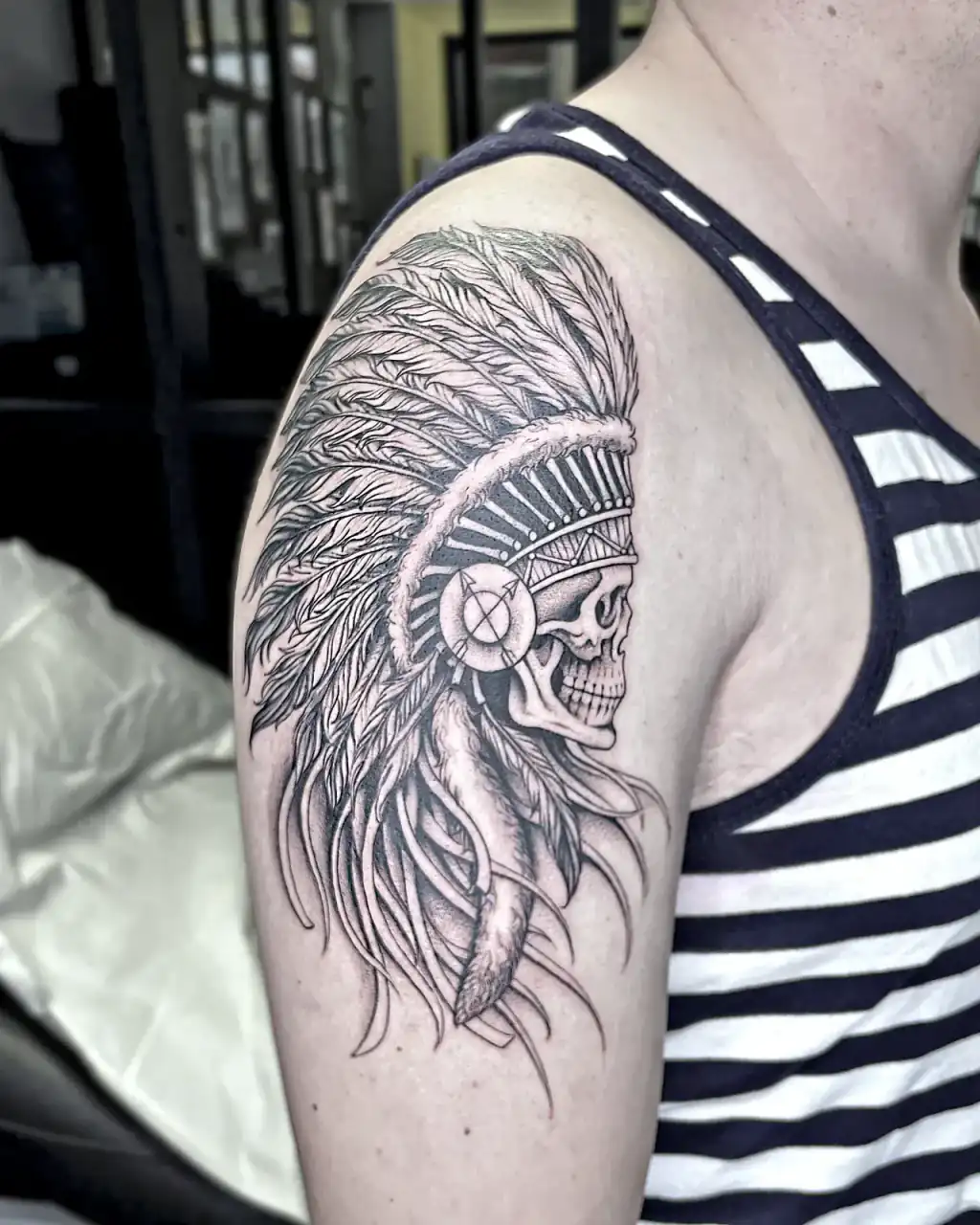 Calavera con tocado de plumas en black and grey sobre el hombro.