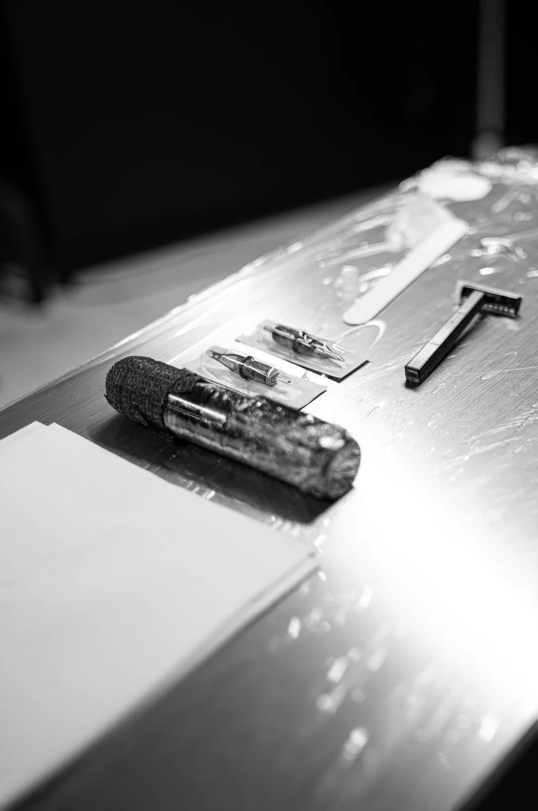 La bandeja preparada antes de empezar: la máquina envuelta, los cartuchos y la cuchilla sobre la mesa forrada. Fotografía en blanco y negro.